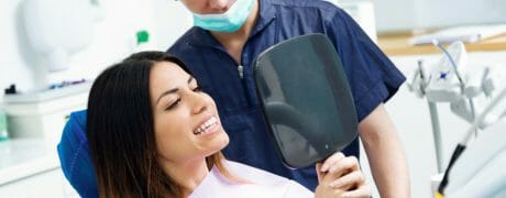 Woman Sitting in Dentist Chair Looking at Teeth in Handheld Mirror